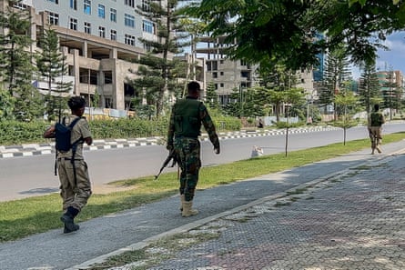 Three soldiers in camouflage and carrying guns walk along a wide city avenue
